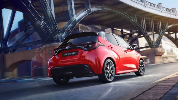 Heckansicht eines roten Yaris Hybrid, der parallel neben einer dunkelgrauen Stahlbrücke fährt.