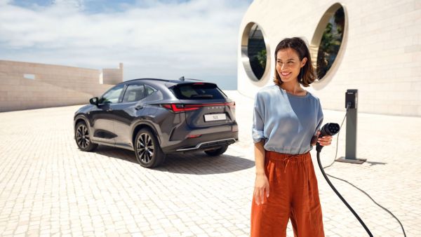 Eine Person steht vor einem in der Sonne geparkten Lexus NX und hält ein Ladekabel in der Hand