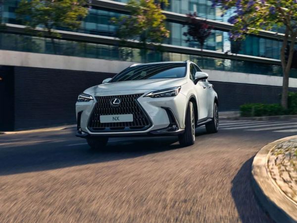 Ein eleganter weißer Lexus NX navigiert durch eine kurvige Straße in einer städtischen Umgebung. 