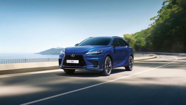 Ein eleganter blauer Lexus RX fährt eine Küstenstraße entlang, mit Blick auf den Ozean und Grünflächen an der Seite