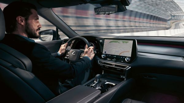 Eine Person am Steuer eines Lexus, die sich auf die Straße konzentriert, während ein GPS-Navigationsbildschirm eine Karte im Armaturenbrett anzeigt.