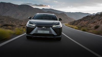 Ein schwarzer Lexus RZ, der auf einer kurvenreichen Straße inmitten einer bergigen Landschaft fährt und Luxus und Abenteuer illustriert.