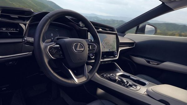 Innenansicht eines Lexus RZ, die das Lenkrad, das Touchscreen-Display und das moderne Design des Armaturenbretts vor einer malerischen Kulisse zeigt.