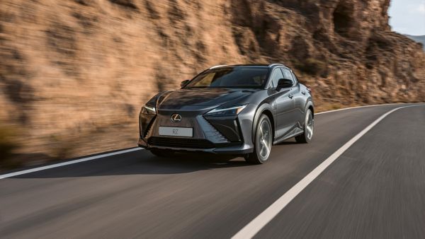 A Lexus RZ 450e driving on a road beside a mountain rock face