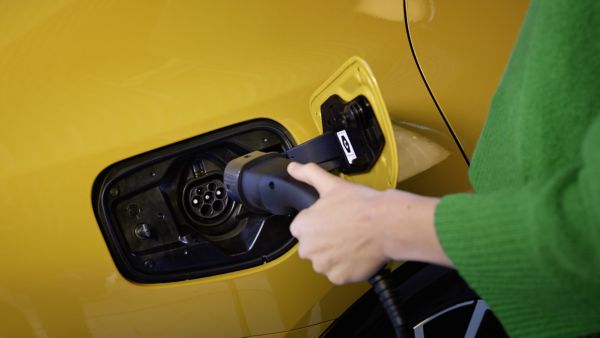 Nahaufnahme einer Person, die ein Ladekabel in die Ladebuchse eines gelben Elektroauto anschließt.