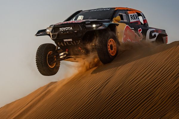 A Toyota GR DKR Hilux Evo powers over the ridge of a sand dune