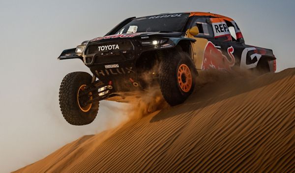 A Toyota GR DKR Hilux Evo powers over a towering sand dune