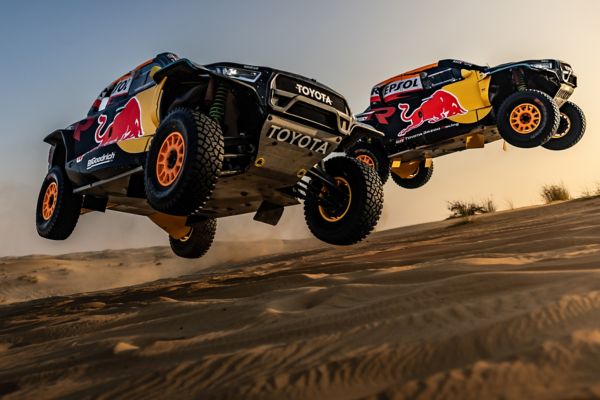 A pair of Toyota GR DKR Hilux Evo racing machines in mid-air in the desert