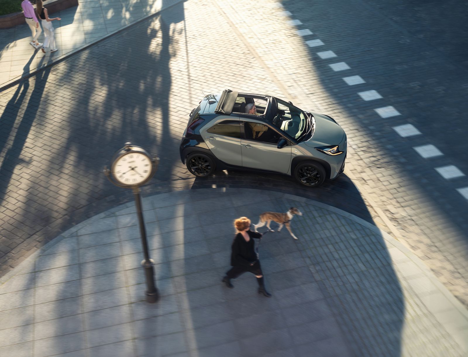 Aygo X parcourt les rues ensoleillées de la ville avec son toit en toile ouvert.
