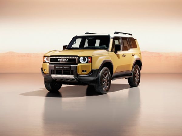 A front view of the all-new Toyota Land Cruiser parked at an angle. Its bright metallic gold paint contrasts with the orange studio setting.