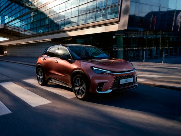 Ein kupferfarbener Lexus LBX fährt durch eine moderne Stadtkulisse