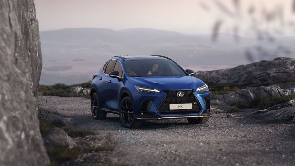 Blauer Lexus NX SUV steht auf einem steinigen Weg in einer bergigen Landschaft bei Sonnenuntergang, umgeben von Felsen und mit Blick auf sanfte Hügel im Hintergrund.