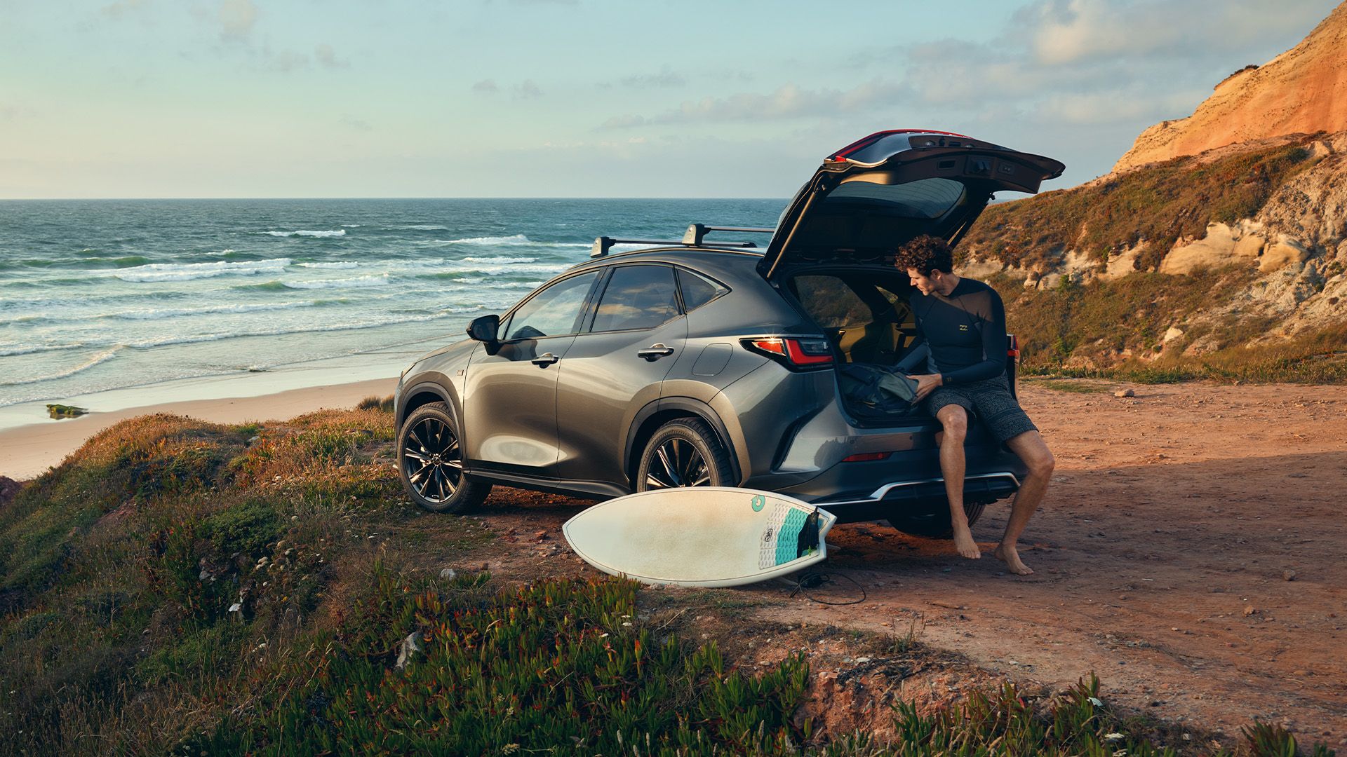 A surfer sat in a boot of a parked Lexus NX at the beach