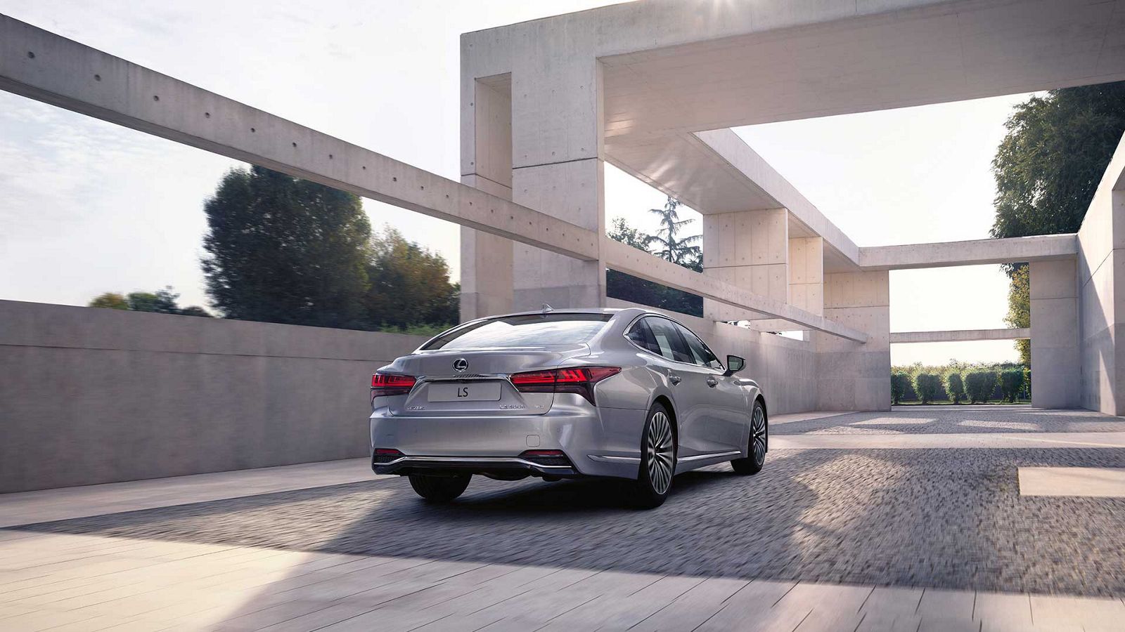 Rear view of a Lexus LS 500h driving alongside a structure