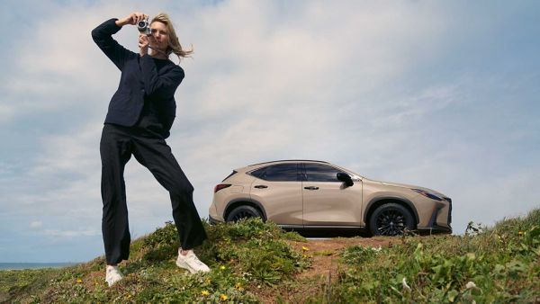 A person taking a photo stood to the side of a parked Lexus NX