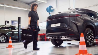 A Lexus mechanic walking past a parked Lexus RZ with a case in hand