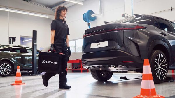 Un meccanico Lexus passa davanti a una Lexus RZ parcheggiata con una valigia in mano