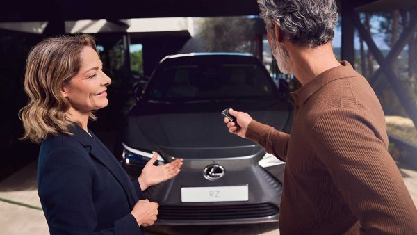 Un employé Lexus se tient à côté d'un client qui tient une clé Lexus RZ