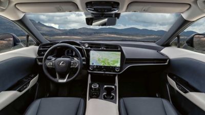 Innenansicht eines Lexus RZ, die das Lenkrad, das Touchscreen-Display und das moderne Design des Armaturenbretts vor einer malerischen Kulisse zeigt.