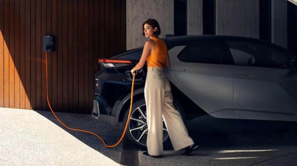 Eine Frau schließt ein orangefarbenes Ladekabel an ihr Elektroauto an, das in einer modernen Garage an einer Wallbox geladen wird. Die Szene zeigt das komfortable E-Auto laden zu Hause – eine beliebte Lademöglichkeit für Elektroautos in Österreich.