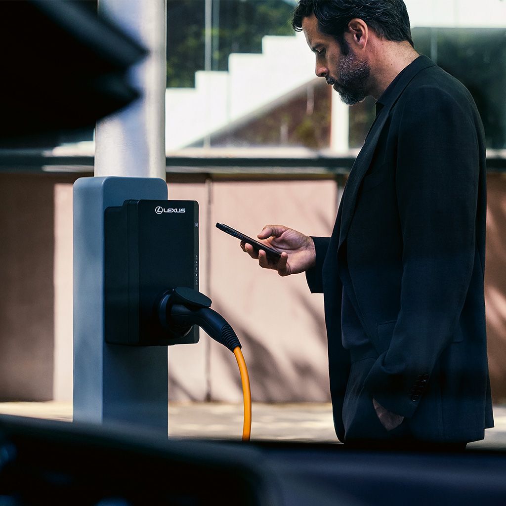 A person standing next to a charging point using the Lexus Link+ app on their mobile phone