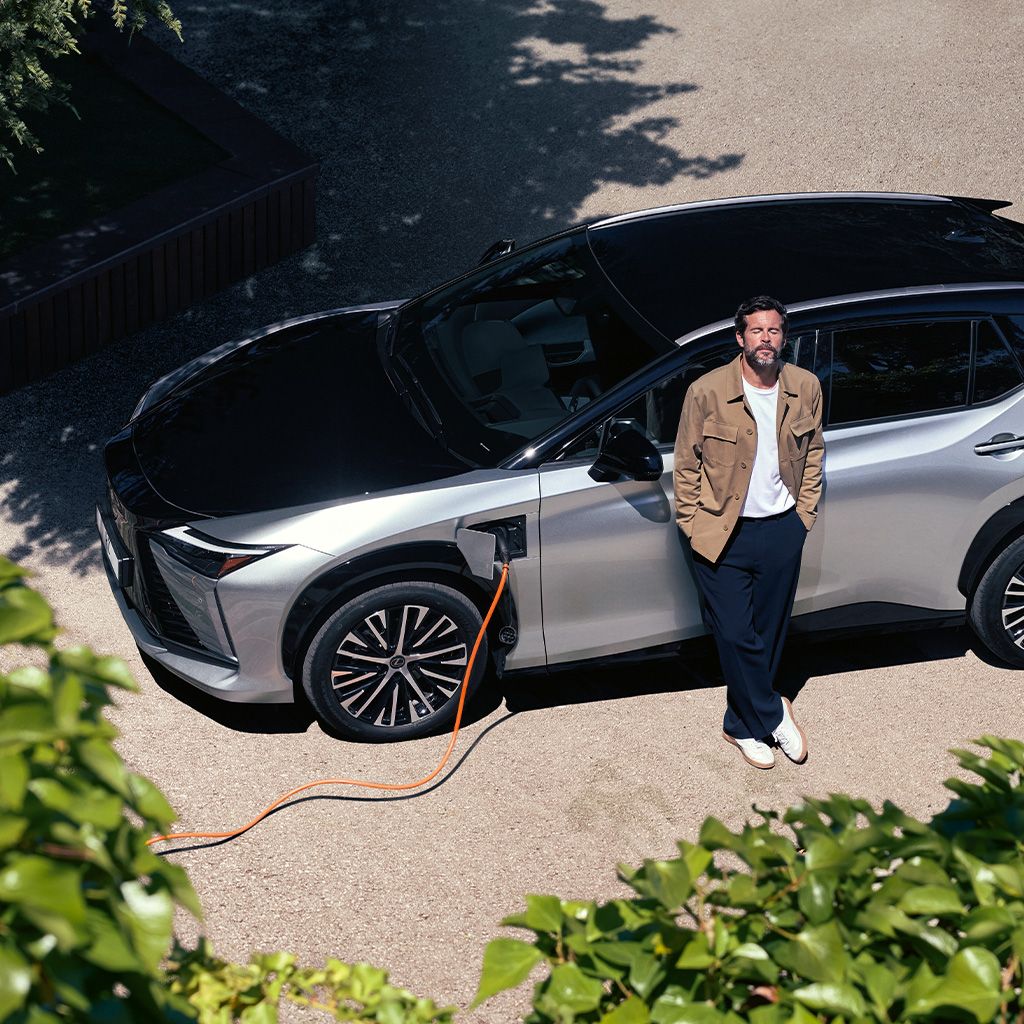 En person, der læner sig op ad en parkeret Lexus RZ