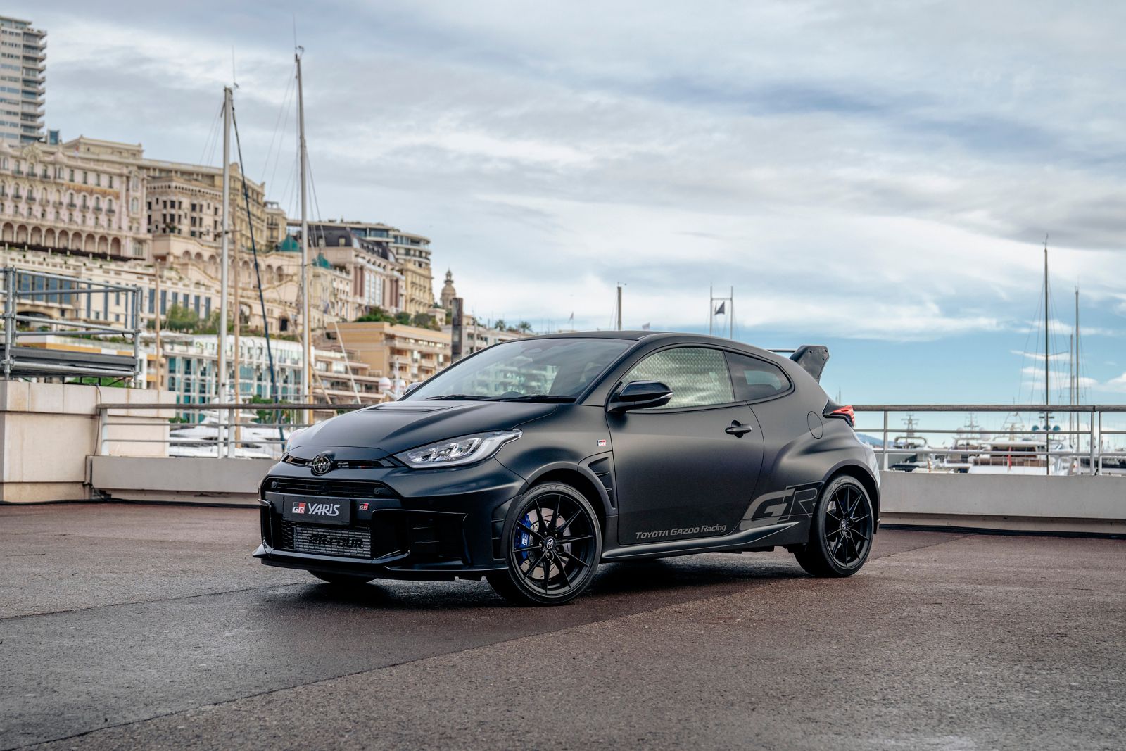 GR Yaris Ogier Edition in mattschwarzer Lackierung von schräg vorn, im Hintergrund Boote im Hafen und städtische Häuser in Monte Carlo
