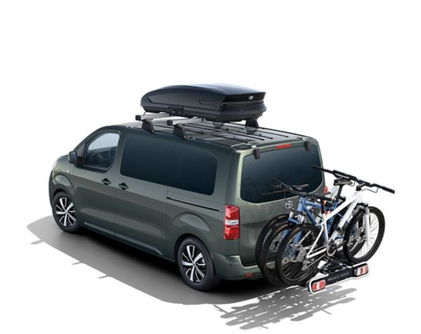 Grüner Proace Verso mit einer Dachbox und einem Fahrradanhänger ausgestattet.