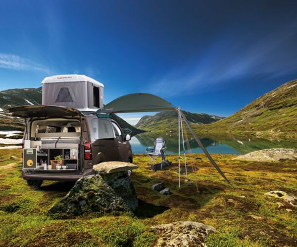 Braun-grauer Toyota Proace Verso mit Camping Ausrüstung steht in einer grünen Landschaft vor einem See