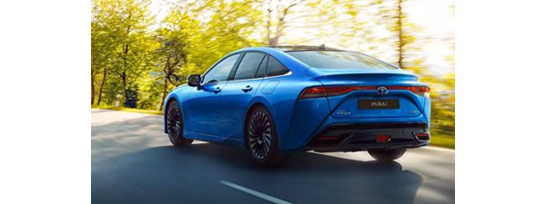Ein blauer Toyota Mirai von hinten, der eine Straße mit Bäumen im Hintergrund entlangfährt.