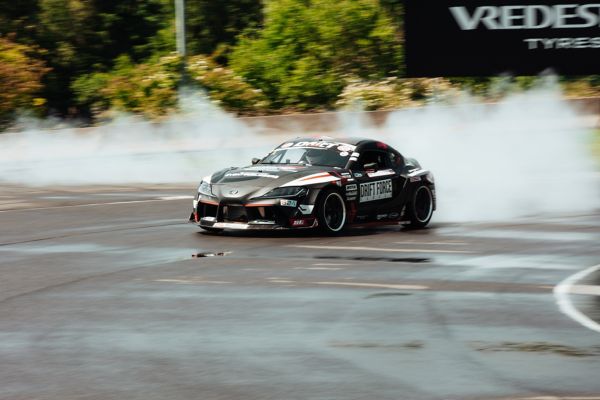 Schwarzer Rennwagen driftet um eine Kurve auf einer Rennstrecke und wirbelt dabei Rauch auf