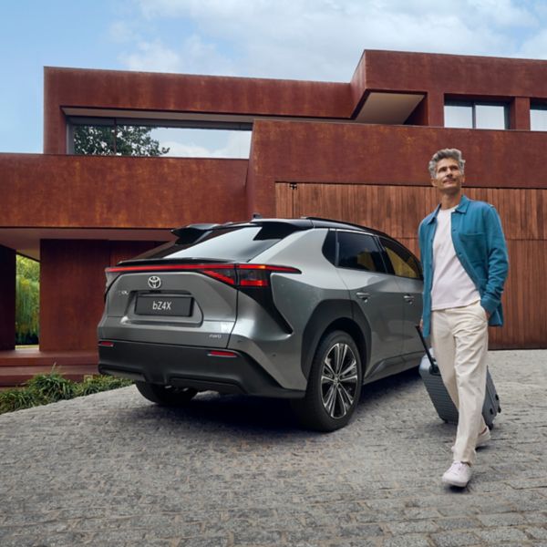 Toyota bZ4x voor een huis met de berijder ernaast