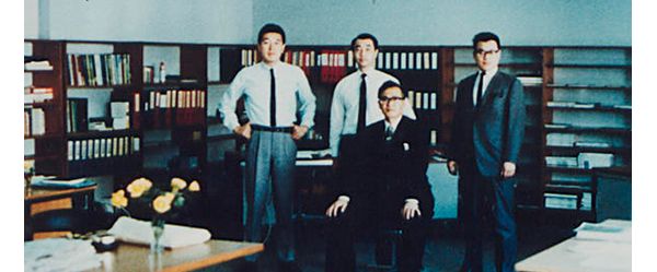 Farbfoto aus den 60er-Jahren: Gruppenbild vier japanischer Männer mit Anzug und Krawatte in einem Büro