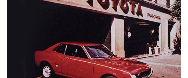 Ein rotes Modell von Toyota aus den 70er-Jahren vor dem Schaufenster eines Toyota Autohauses