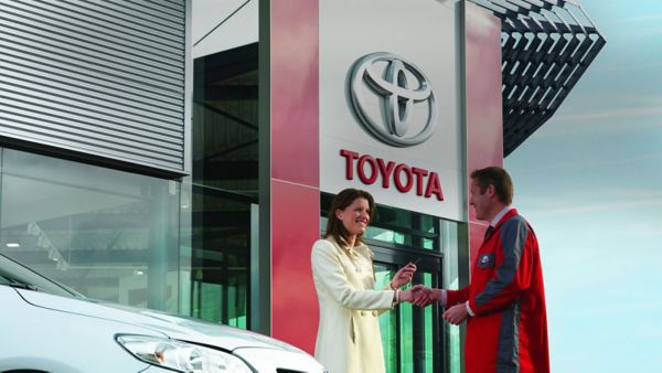 Zwei Personen stehen vor einen Toyota Autohaus und schütteln die Hände