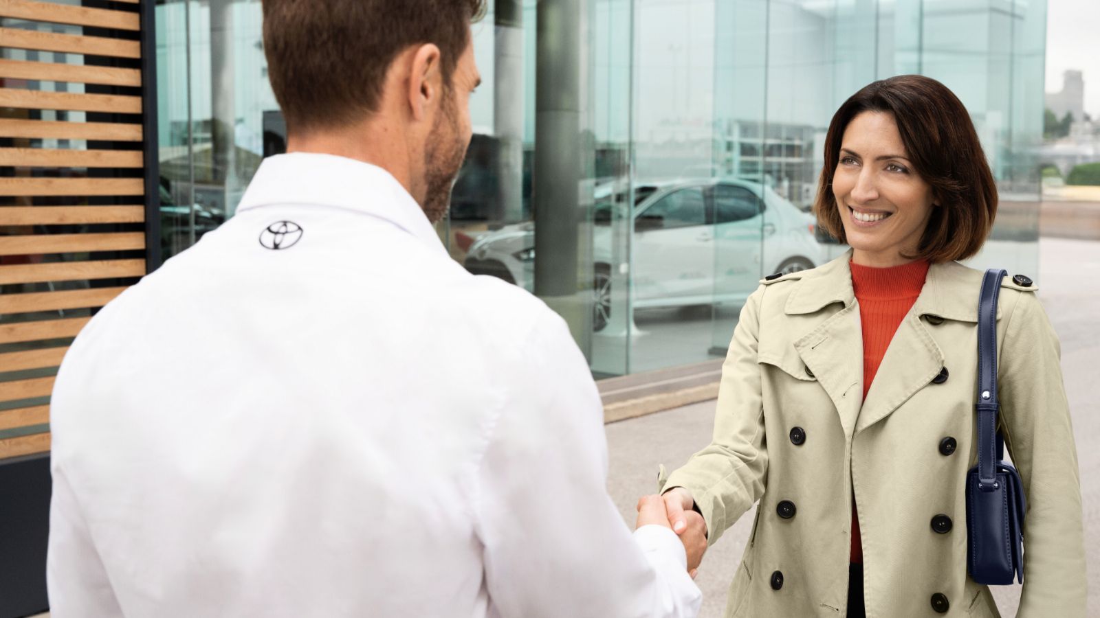 Uśmiechnięta kobieta podaje i pracownik salonu Toyoty podają sobie dłonie.