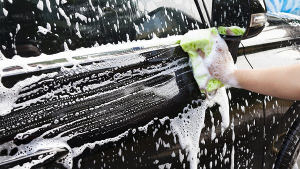 Nahaufnahme einer manuellen Handwäsche mit Schwamm und Schaum an der Tür eines Fahrzeugs.