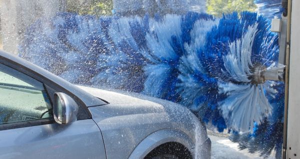 Auto in der Waschanlage während der Reinigung mit rotierenden Bürsten und starkem Wasserstrahl.