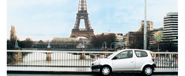 Foto aus den 80er-Jahren: ein silberner Toyota Yaris geparkt auf einer Brücke, im Hintergrund der Eiffelturm