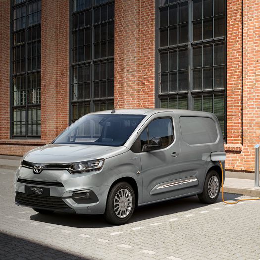 Stříbrná elektrická dodávka Toyota Proace City Electric nabíjí se u cihlové budovy.