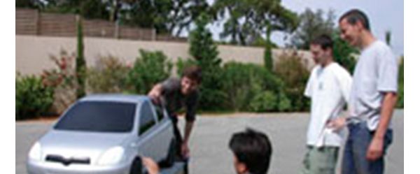 Vier junge Männer begutachten im Freien das silberne Modell eines Toyota Yaris.