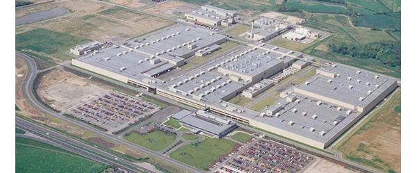 Luftaufnahme einer großen Autofabrik, daneben ein Parkplatz mit Autos sowie eine Autobahn