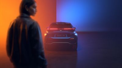 Eine Person geht an einem Toyota C-HR vorbei, der in farbigem Licht inszeniert ist.