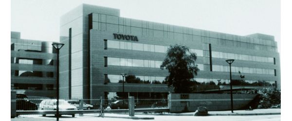 Schwarz-Weiß-Foto von 1993: Außenaufnahme eines vierstöckigen Bürogebäudes mit Toyota Schriftzug, davor Autos auf dem Parkplatz