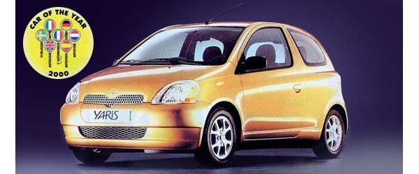 Ein gelber Toyota Yaris von 1999 vor dunklem Hintergrund, daneben ein gelbes Logo mit der Aufschrift „Car of the year 2000“