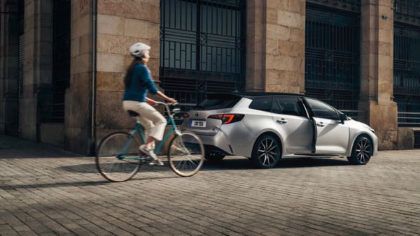 Woman biking by Toyota Corolla Touring Sports parked