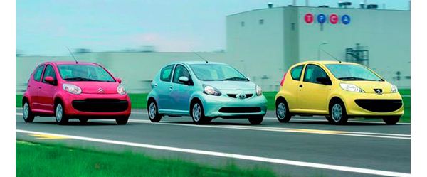 Ein mintgrüner Toyota Yaris zwischen einem baugleichen roten Citroen und einem gelben Peugeot auf einer Teststrecke vor einer Fabrikhalle