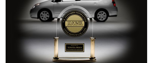 Trophäe eines Preises für Kundenzufriedenheit für den Toyota Prius, speziell ausgeleuchtet, im Hintergrund ein silberner Prius aus den 2000er-Jahren 