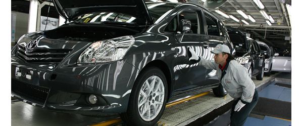 Ein Fabrikarbeiter mit weißen Handschuhen prüft bei der Endabnahme eines gerade produzierten grauen Toyotas auf dem Fließband den Lack an der Fahrertür