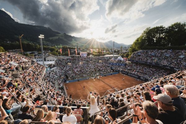 Eine Tennisarena in Kitzbühel, im Hintergrund scheint die Sonne durch die Berge